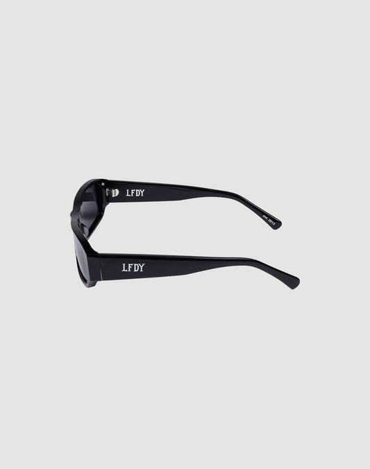 The LFDY Wrap sunglasses by LIVE FAST DIE YOUNG feature thick black frames, colored lenses, and the white LFDY logo on the temples, displayed from the side against a plain light gray background.