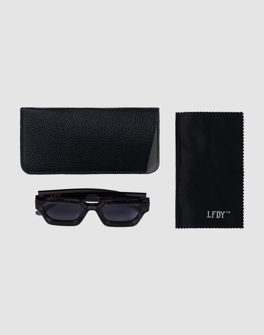 The LFDY Big Wire black rectangular sunglasses by LIVE FAST DIE YOUNG, a textured black case, and a black LFDY™ cleaning cloth are displayed neatly on a light gray background.