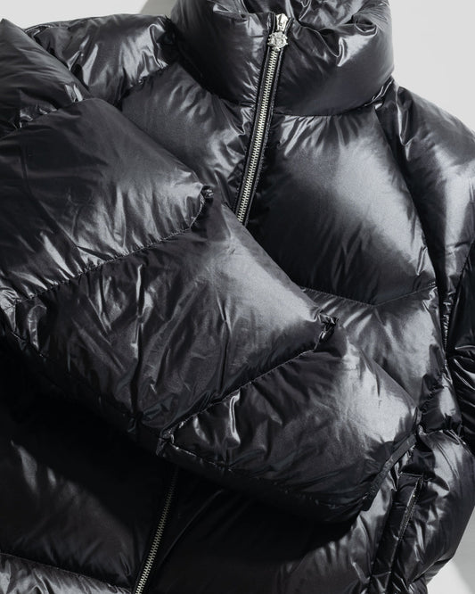 Close-up of the shiny black Live Fast Down Jacket by LIVE FAST DIE YOUNG, featuring a visible front zipper and quilted sections. The glossy, water-repellent fabric reflects light, accentuating its puffy texture and modern style.