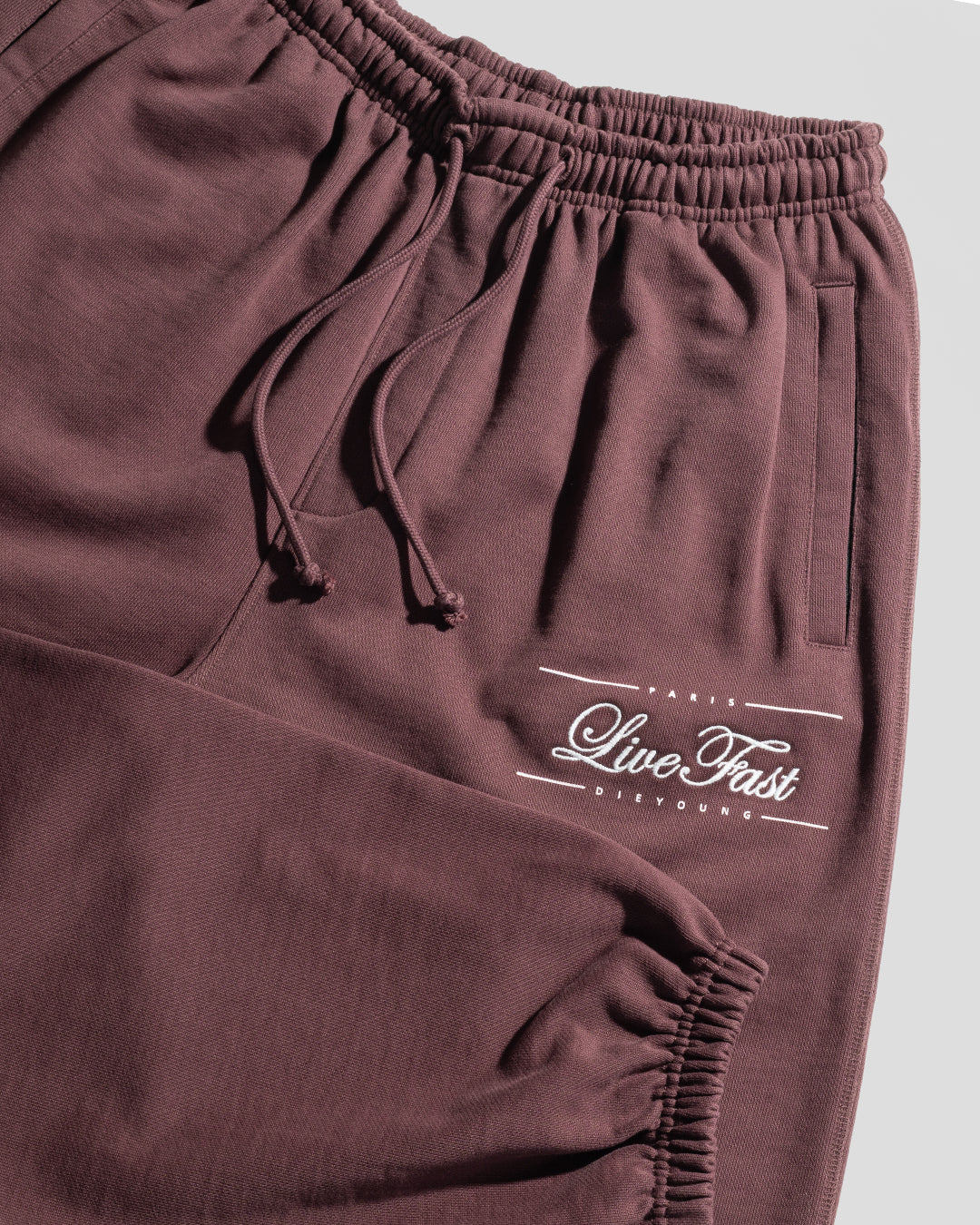 LIVE FAST DIE YOUNG Wide Cuff Jogger: maroon, wide fit, soft French Terry (100% Baumwolle), elastic waistband with drawstrings, side pockets, and "Live Fast" in white script on the upper thigh.