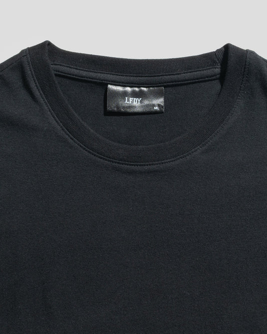 Close-up of a plain black LFDY Slim Tee by LIVE FAST DIE YOUNG, lying flat to reveal the upper chest and neckline. A black label with "LFDY" text is visible inside the collar. The shirt is crafted from soft cotton.