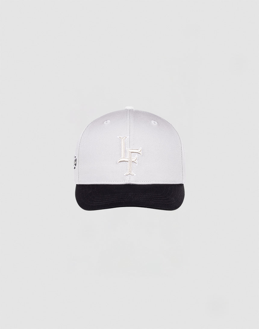 The LF Snapback by LIVE FAST DIE YOUNG features a white cap with a white LF logo, black brim with black underside, and snap closure, shown on a plain light gray background.