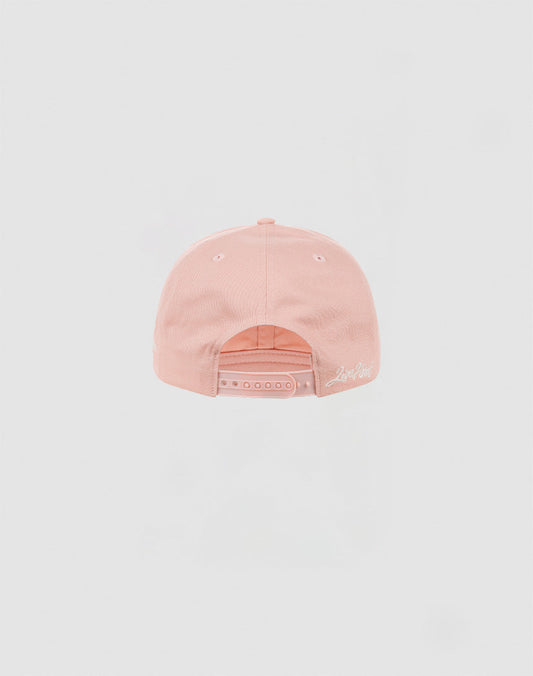 The LF Snapback by LIVE FAST DIE YOUNG is a light pink cotton baseball cap, shown from the back with a snap closure and white embroidered logo in script near the edge.