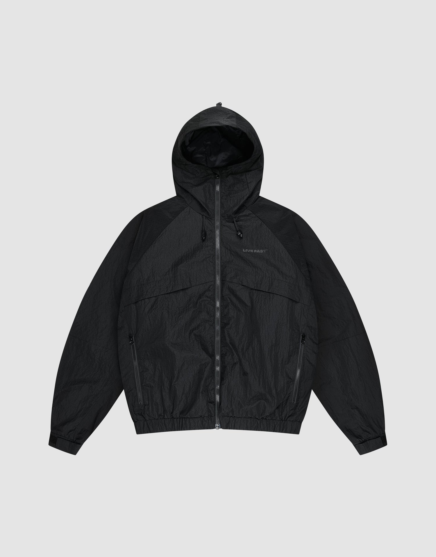 The LIVE FAST DIE YOUNG Live Fast Nylon Jacket is a black, oversized zip-up windbreaker with long sleeves, hood, Stehkragen, and side pockets, shown against a plain light gray background. | plain