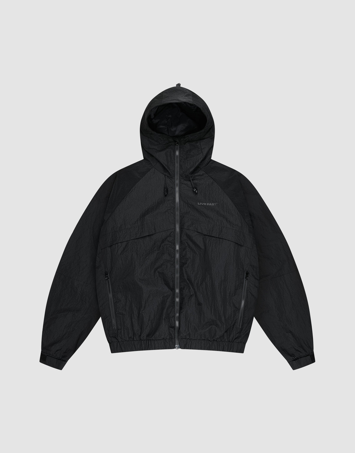 The LIVE FAST DIE YOUNG Live Fast Nylon Jacket is a black, oversized zip-up windbreaker with long sleeves, hood, Stehkragen, and side pockets, shown against a plain light gray background. | plain