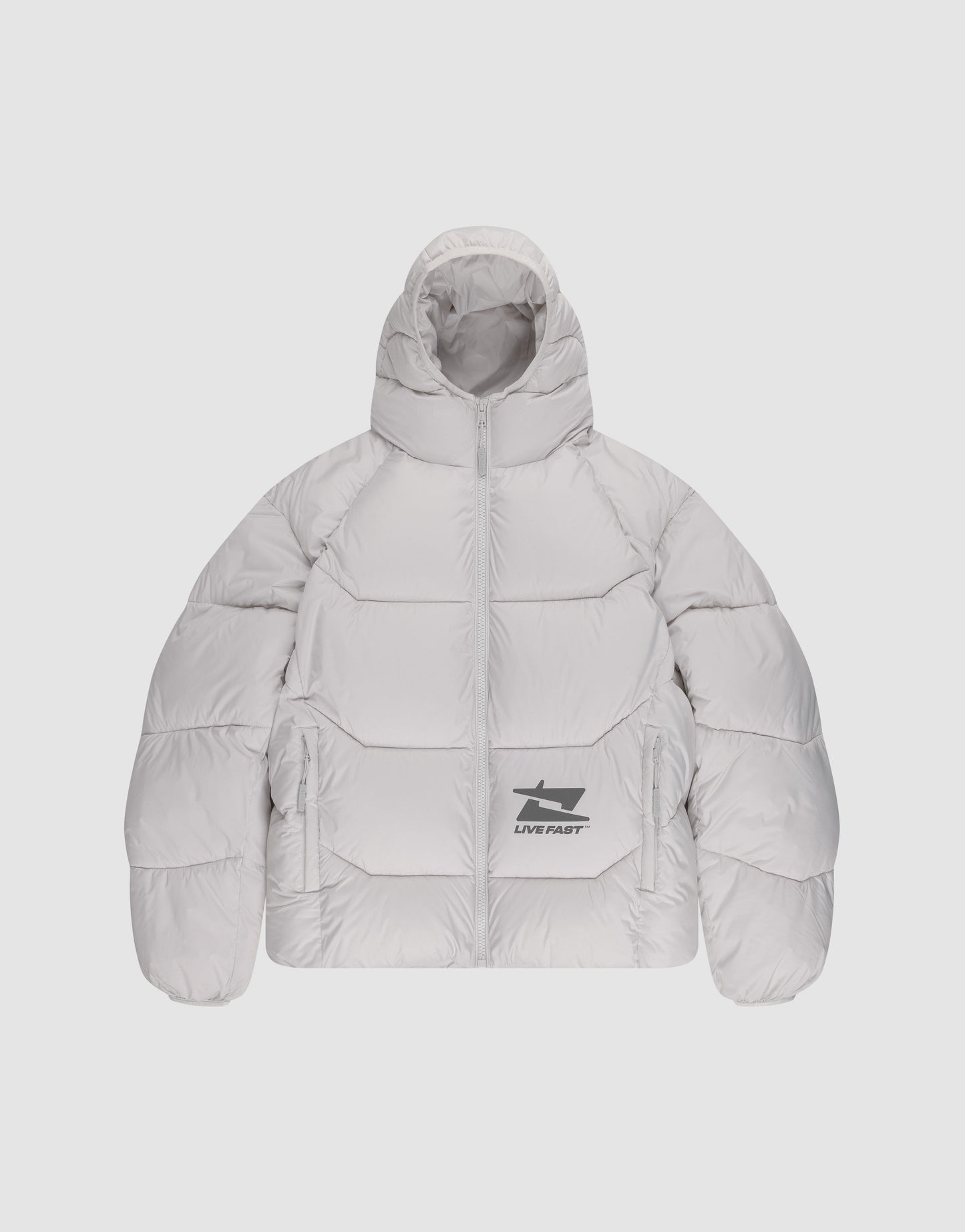 A person stands against a plain background wearing the LIVE FAST DIE YOUNG Live Fast Puffer Jacket in light gray with an oversize fit and water-repellent finish, paired with matching gloves, a beanie, loose black pants, and white sneakers.