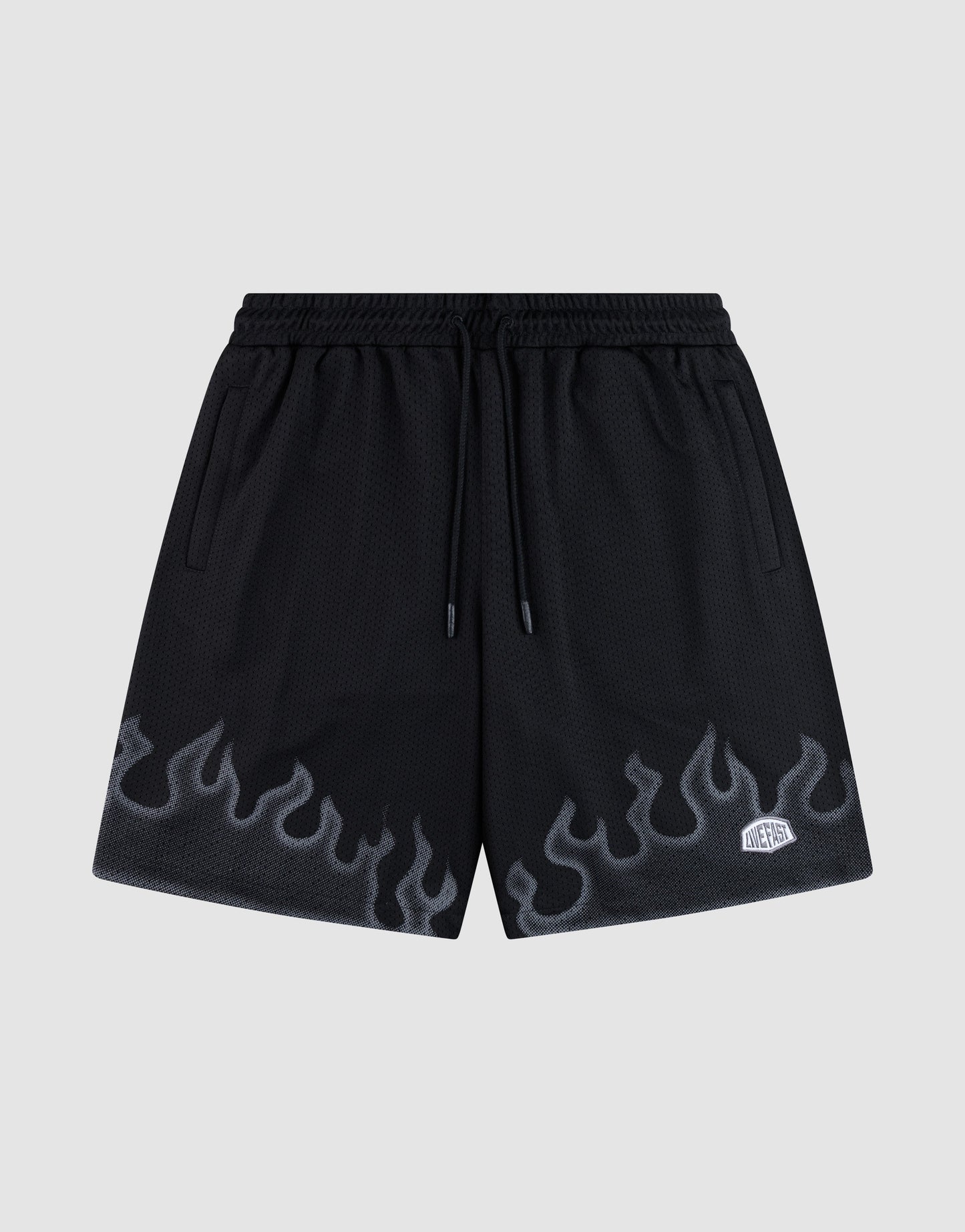 LIVE FAST DIE YOUNG Burning Mesh Shorts: black athletic shorts with elastic waistband, drawstring, gray flame print along the bottom, and a small white rectangular patch on the left leg. Plain light gray background. | plain