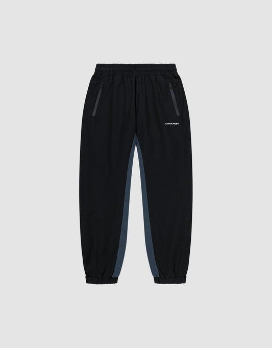 Black Basic Shell Pants by LIVE FAST DIE YOUNG with elastic waistband, zippered side pockets, gray panels, and elastic cuffs. Features a white reflective logo on the left thigh. Displayed on a plain light background. | plain