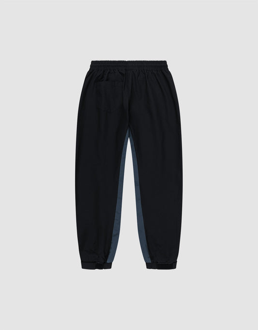 The LIVE FAST DIE YOUNG Basic Shell Pants are black jogger-style trousers with an oversize fit, Elastikbund, a right back pocket, and grey side panels, shown on a light grey background.