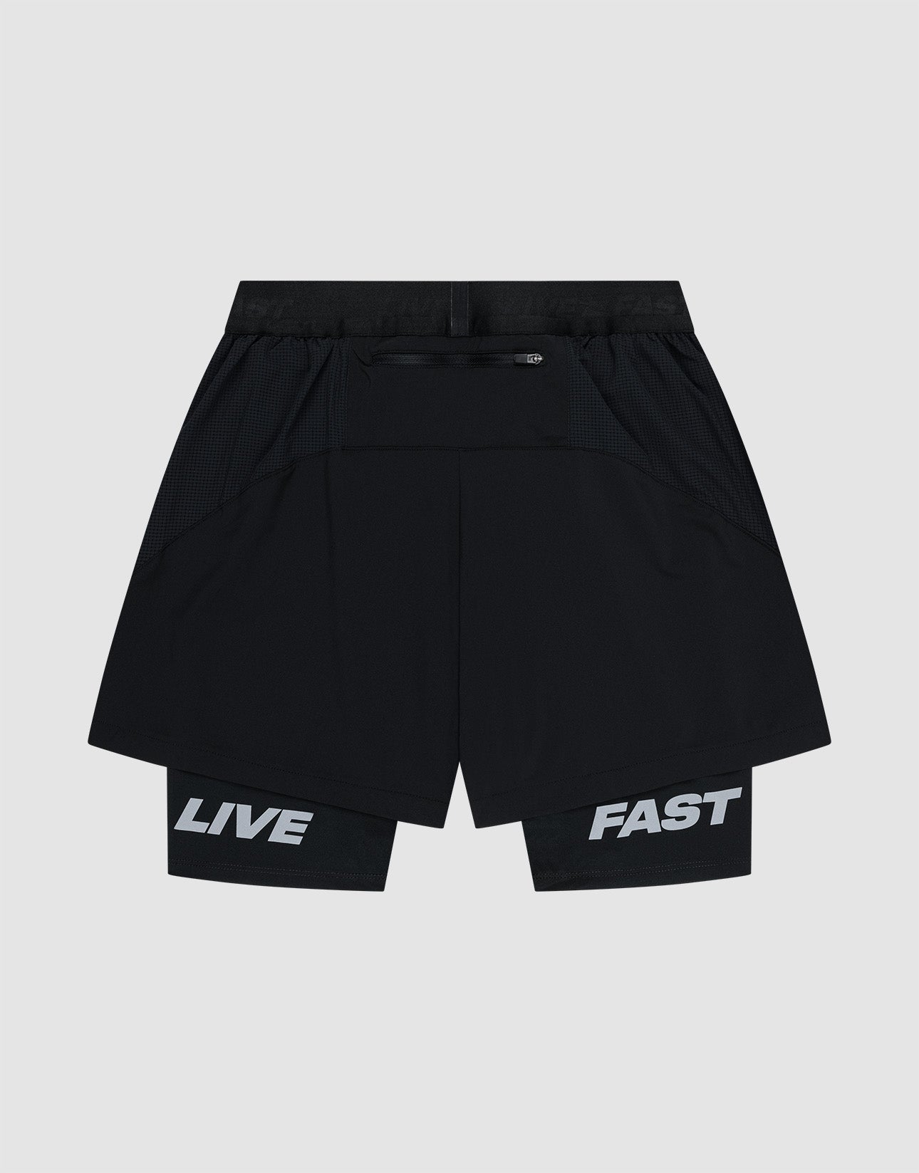 A man with braided hair, white socks, and sneakers faces away wearing LIVE FAST DIE YOUNGs black Live Fast Performance Running Shorts (Regular Fit) featuring LIVE on the left leg and FAST on the right, plus a black long-sleeve shirt.