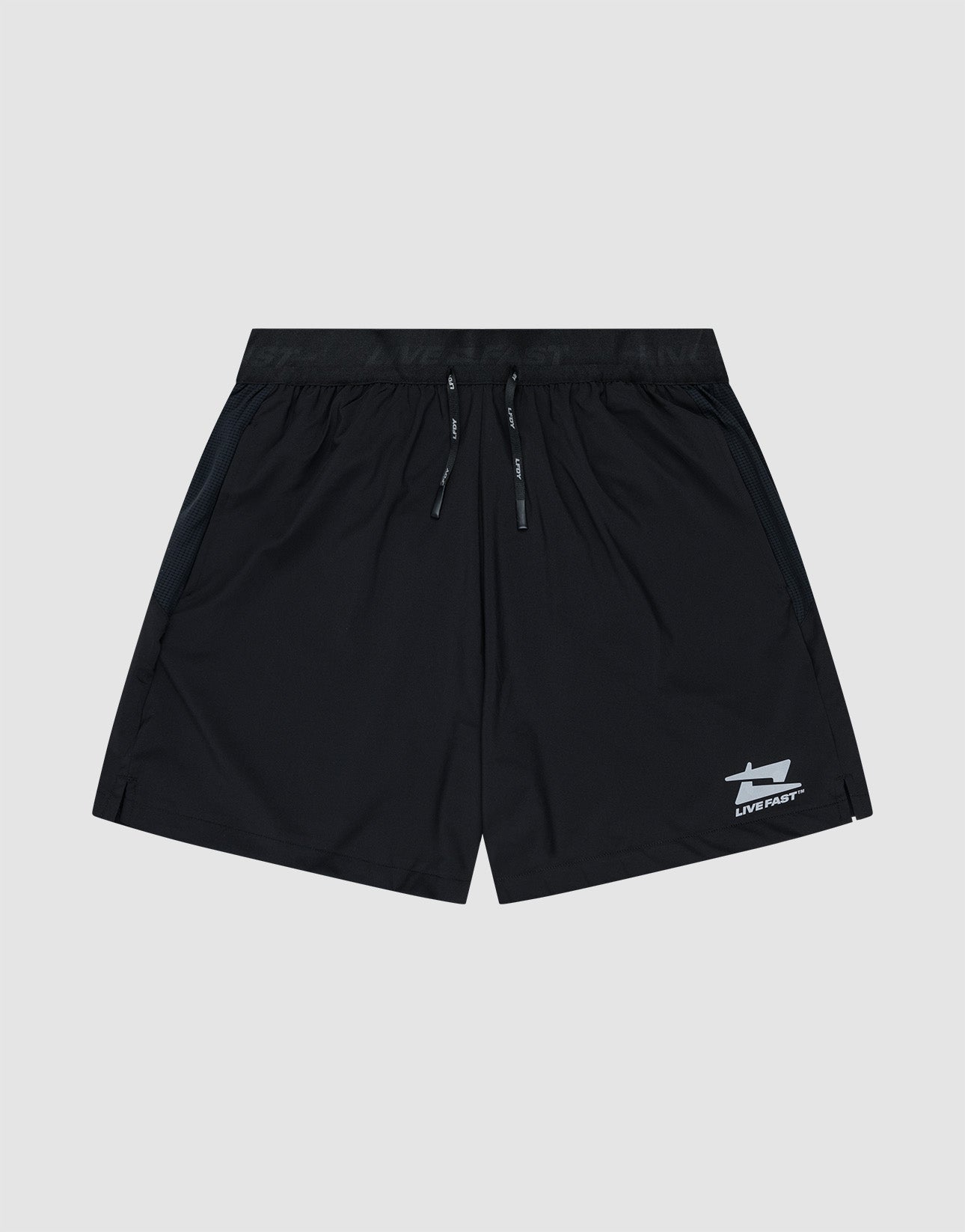 A model wears LIVE FAST DIE YOUNGs Live Fast Performance Shorts with a reflective LIVE FAST waistband, paired with white socks and sneakers, standing against a plain white background.