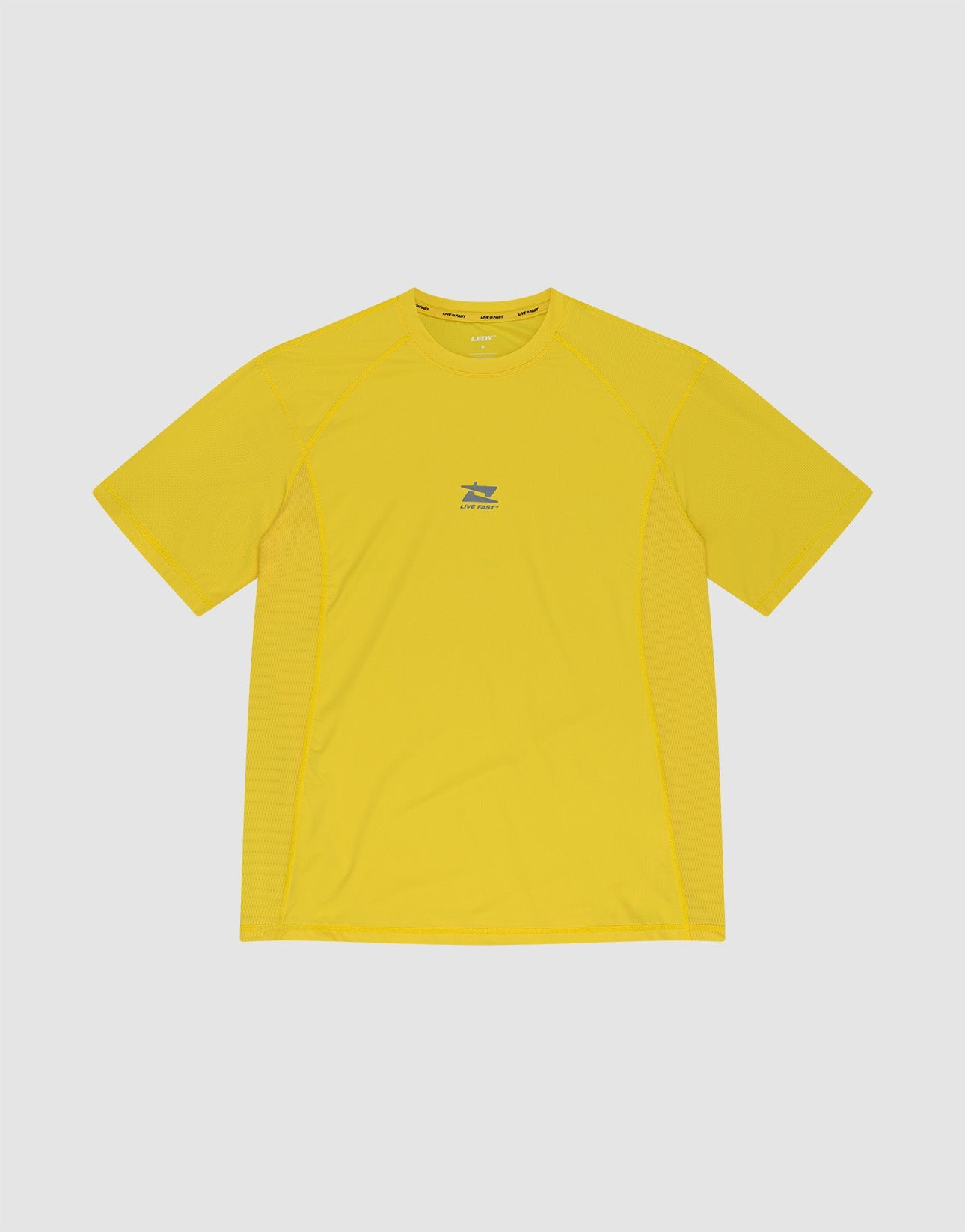 A man stands against a plain light background wearing the LIV FAST DIE YOUNG Live Fast Performance Tee in bright yellow with matching shorts, both made from comfortable Nylon Spandex. He looks to his left with one hand by his side, paired with white socks and sneakers.