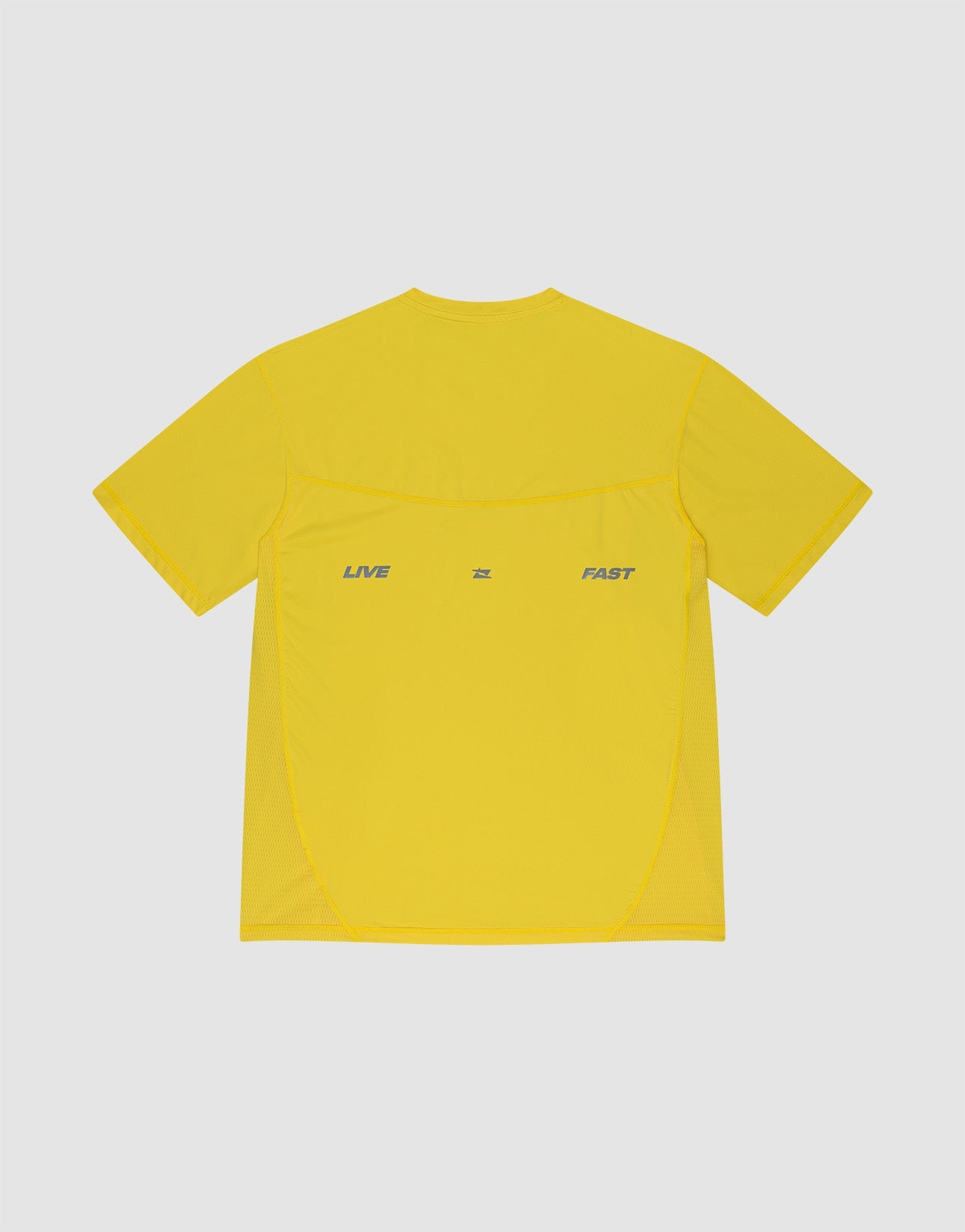 A man faces away from the camera in a slim-fit, bright yellow Live Fast Performance Tee by LIVE FAST DIE YOUNG, paired with matching shorts featuring LIVE and FAST, plus white socks and shoes. Reflective print details pop against a plain background.