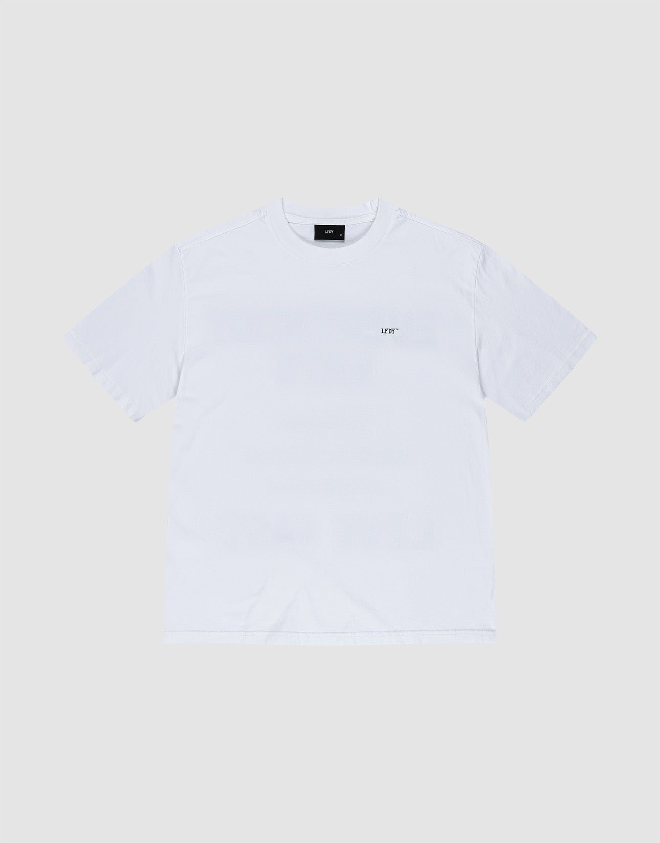 A man wearing sunglasses and the LIVE FAST DIE YOUNG Everybody Eats Tee—an Oversize Fit white T-shirt with green and yellow Backprint made from 100% Baumwolle—plus yellow shorts, white socks, and sneakers stands facing away from the camera.