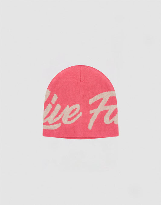 The LFDY Jacquard Beanie by LIVE FAST DIE YOUNG is a pink polyacryl hat with a large cream cursive logo wrapping around it, displayed on a plain light gray background.| plain 