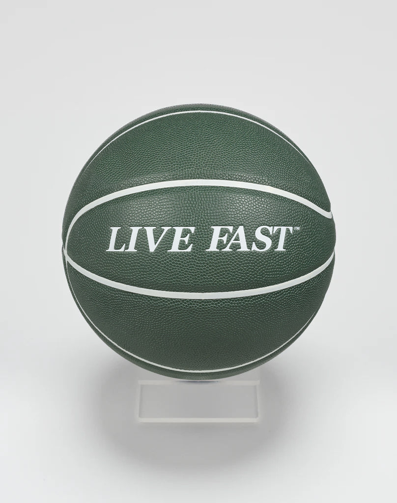 A dark green Live Fast Basketball by LIVE FAST DIE YOUNG, featuring bold white LIVE FAST lettering and white stripes, displayed on a clear stand against a plain white background.| plain 