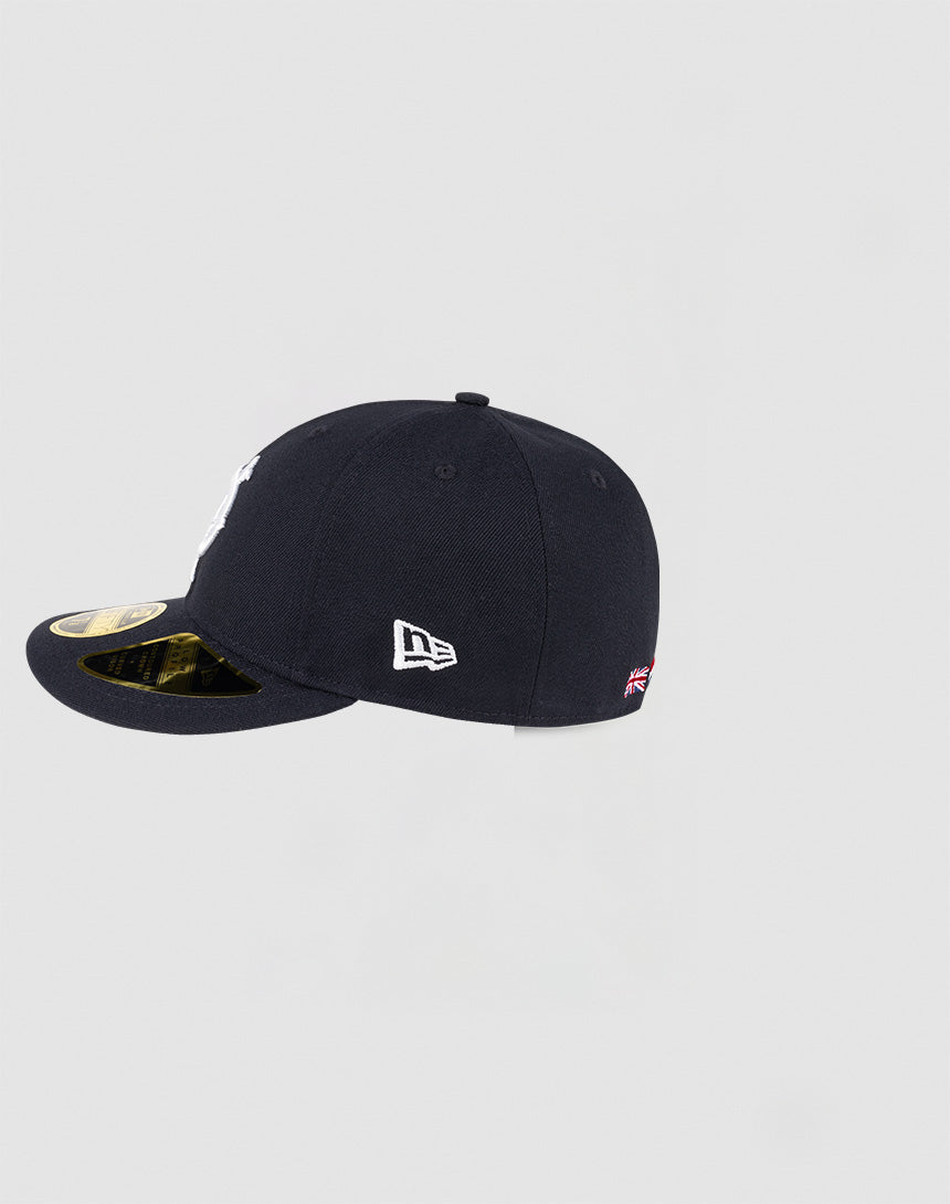 The LFDY x NEW ERA 59FIFTY Low Profile cap by LIVE FAST DIE YOUNG is navy with a flat brim, features a white New Era logo on the side, a small UK flag patch near the back, and sports a gold sticker on the brim.