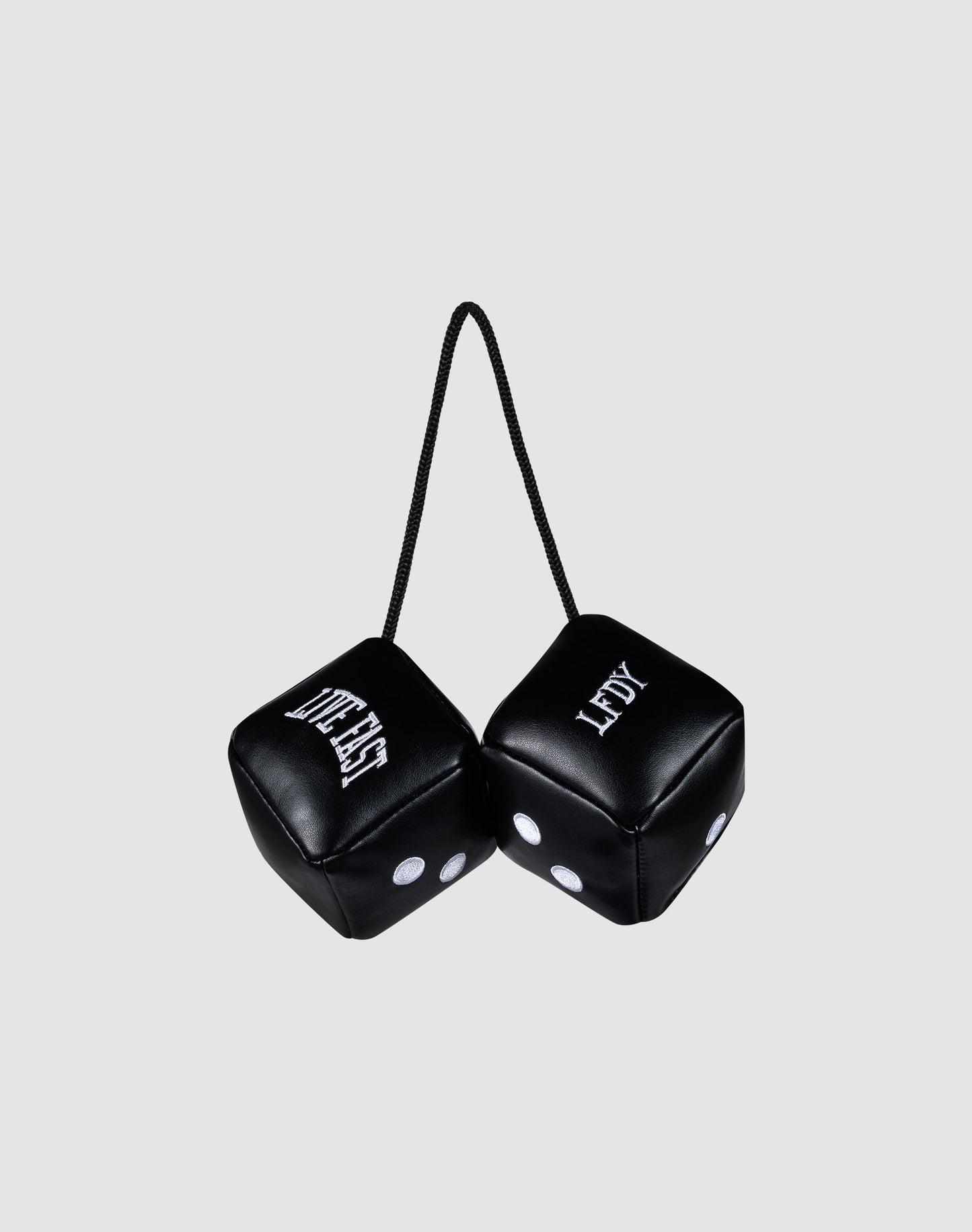 Two black LFDY Leather Car Dice by LIVE FAST DIE YOUNG, connected by a black string, hang from your rearview mirror. Both display "LEFTY" with white dots and lettering against a plain light gray background.| plain 