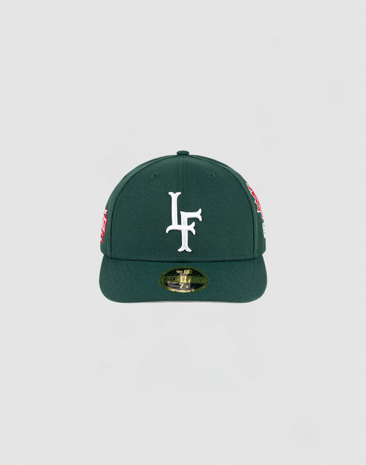 The LFDY x NEW ERA 59FIFTY Low Profile by LIVE FAST DIE YOUNG is a dark green fitted cap with a flat brim, large white LF logo on the front, side patches, and a gold sticker on the brim.