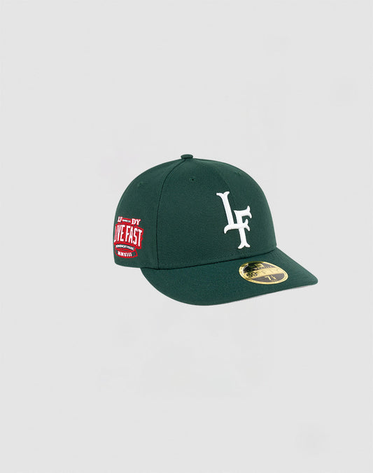The LFDY x NEW ERA 59FIFTY Low Profile by LIVE FAST DIE YOUNG is a dark green fitted cap with a white LF logo front, red LIVE FAST side patch, and gold brim sticker, displayed on a plain light gray background.