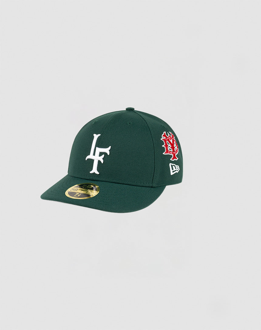 The LFDY x NEW ERA 59FIFTY Low Profile fitted cap by LIVE FAST DIE YOUNG comes in dark green with a white LF logo, red and white side embroidery, and a gold brim sticker, displayed against a plain light background.