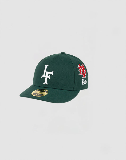 The LFDY x NEW ERA 59FIFTY Low Profile fitted cap by LIVE FAST DIE YOUNG comes in dark green with a white LF logo, red and white side embroidery, and a gold brim sticker, displayed against a plain light background.