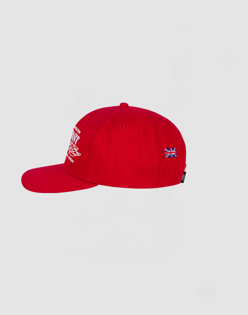The Live Fast Corporation Cap by LIVE FAST DIE YOUNG is a bright red 100% cotton cap, shown from the side with a small embroidered Union Jack on the left and partially visible white front text, set against a plain light gray background.