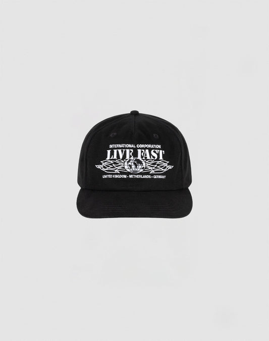 The Live Fast Corporation Cap by LIVE FAST DIE YOUNG is a black, 100% cotton unstructured 5-panel hat with multi-logo white text and graphics reading INTERNATIONAL CORPORATION LIVE FAST above stylized wings and UNITED KINGDOM - NETHERLANDS - GERMANY below.