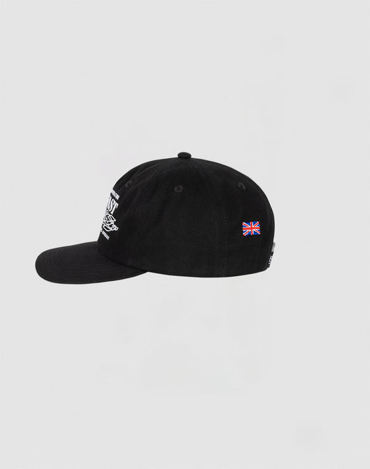 The LIVE FAST DIE YOUNG Live Fast Corporation Cap is a black 5-panel cotton cap with white front embroidery, multi-logo details, and a small Union Jack flag patch on the side, shown against a plain white background.