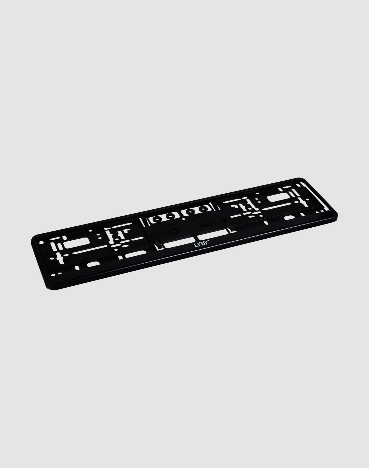 The LFDY License Plate Holder (2 Pack) by LIVE FAST DIE YOUNG is a black plastic Eurokennzeichen holder with multiple mounting slots and holes and a subtle LFDY logo, shown on a light gray background.| plain 