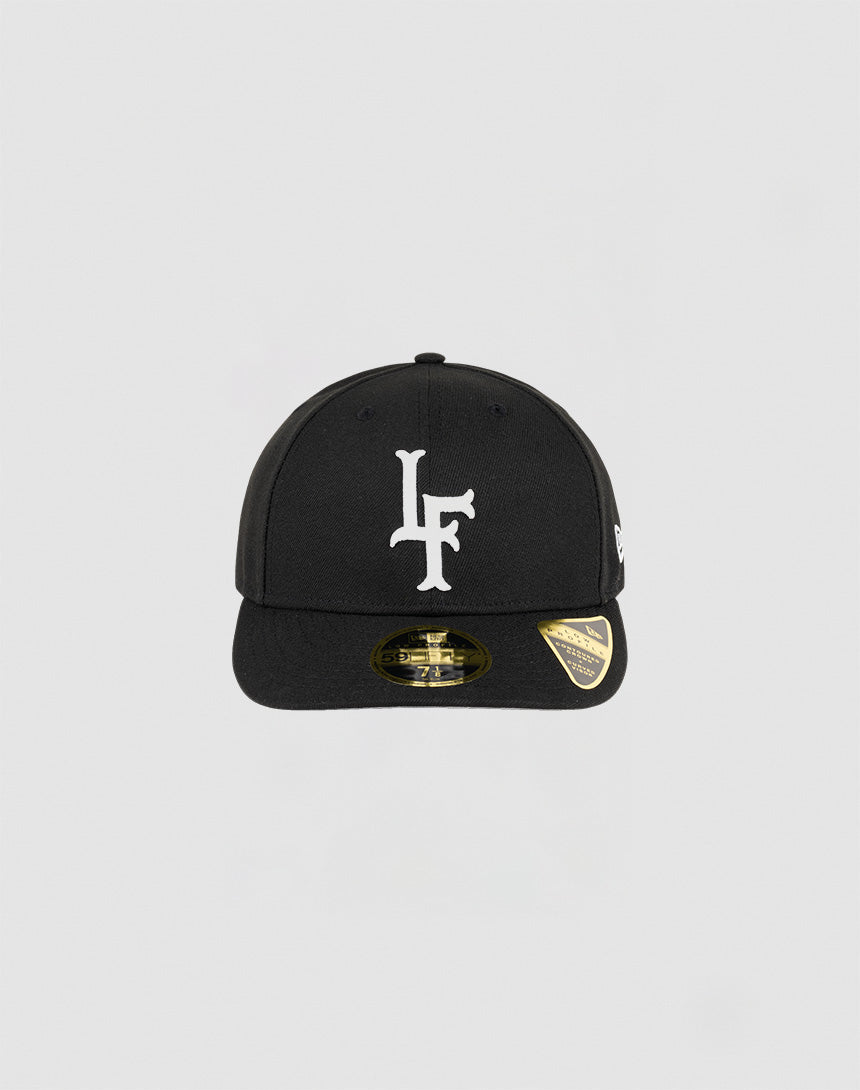 The LFDY x NEW ERA 59FIFTY Low Profile by LIVE FAST DIE YOUNG is a black fitted cap with a white LF logo on the front, gold sticker on the brim, and small white side logo, shown against a plain light gray background.| plain