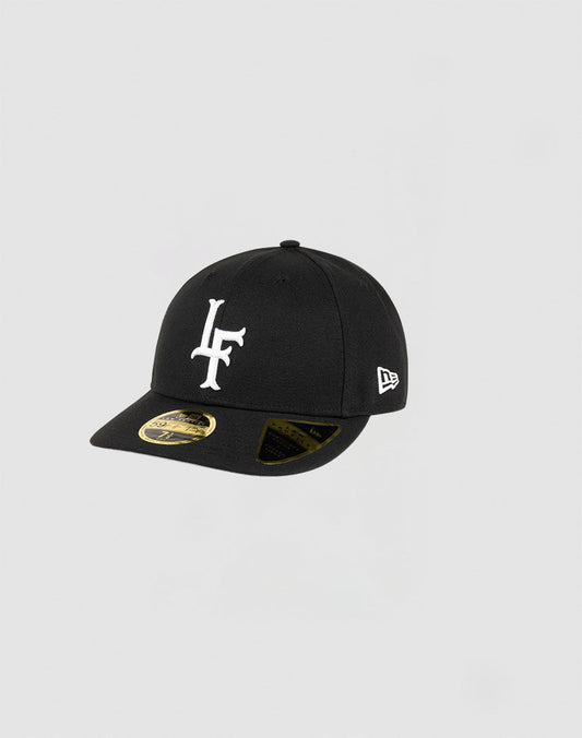 The LFDY x NEW ERA 59FIFTY Low Profile Fitted Cap by LIVE FAST DIE YOUNG features a black design, curved brim, bold white LF logo front, New Era side logo, official stickers on the brim, and a modern low profile silhouette.